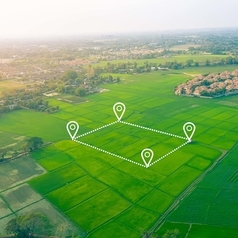 Luftaufnahme eines Ortes mit Feldern davor auf denen symbolisch ein Grundstück abgesteckt ist.