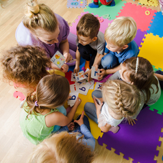 Mehrere Kinder sitzen mit einer Erzieherin auf einer Puzzlematte und spielen.