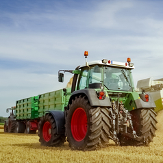 Ein Mähdrescher und ein Traktor bei der Getreideernte auf einem Feld.