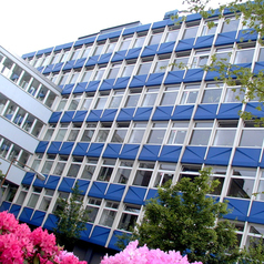 Ausschnitt des blauen LSN-Gebäudes mit Bäumen und Blumen im Vordergrund