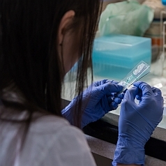 Eine Laborantin sitzt an einem Labortisch und beschriftet ein Reagenzglas.