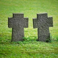 Zwei kreuzförmige Grabsteine stehen auf einer grünen Wiese.