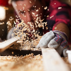 Ein Handwerker hobelt Holz und Späne fliegen durch die Luft.