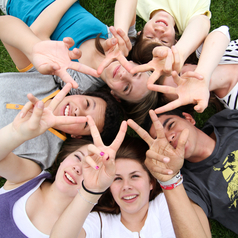 Mehrere Jugendliche liegen auf dem Rasen und machen das Victory-Zeichen mit den Händen.